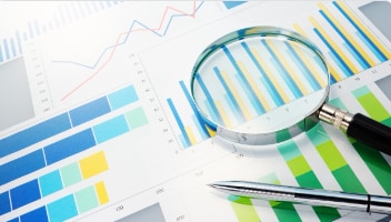 Photo of a magnifying glass with charts on a table.