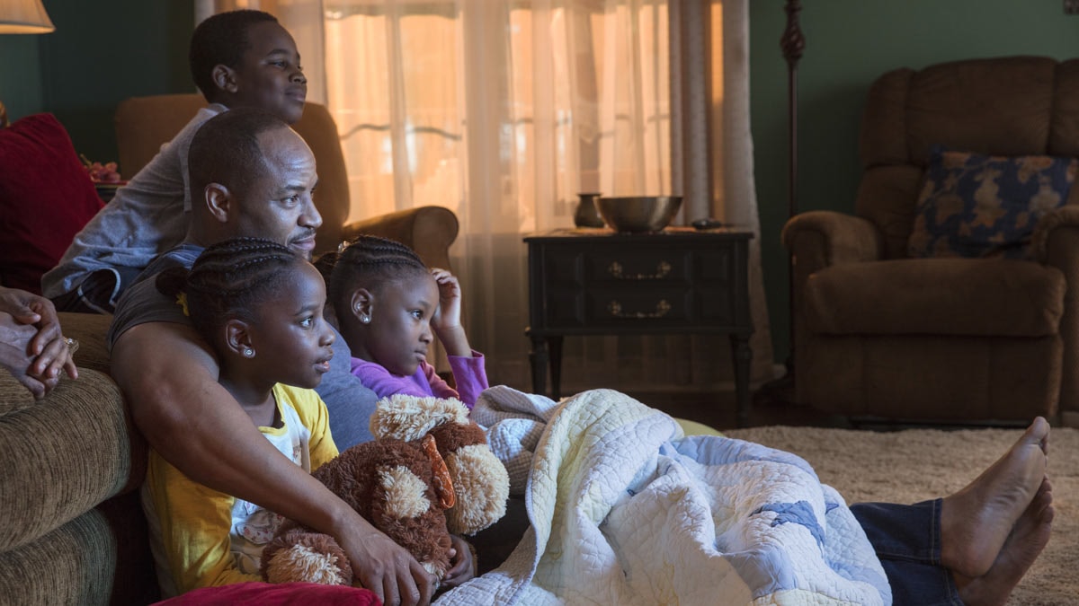 Father and 3 kids watching a movie together in living room