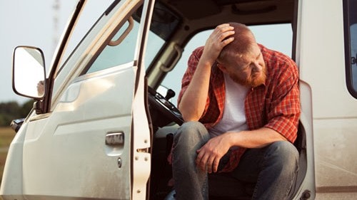 Photo of a man sitting on a van with its door open.