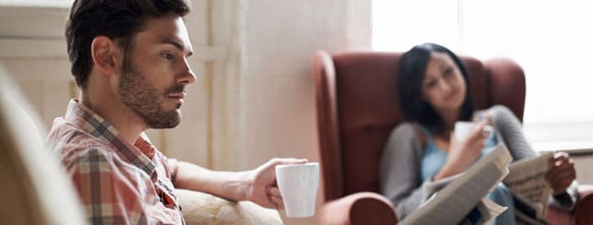 Man and woman sitting looking at newspaper while holding coffee cups