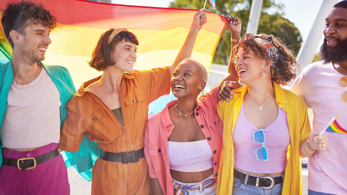 Young men and women wearing a variety of bright colors holding a rainbow pride flag