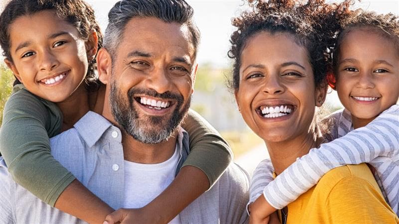 A smiling family, with the son on his father's back and the daughter on the mother's back.