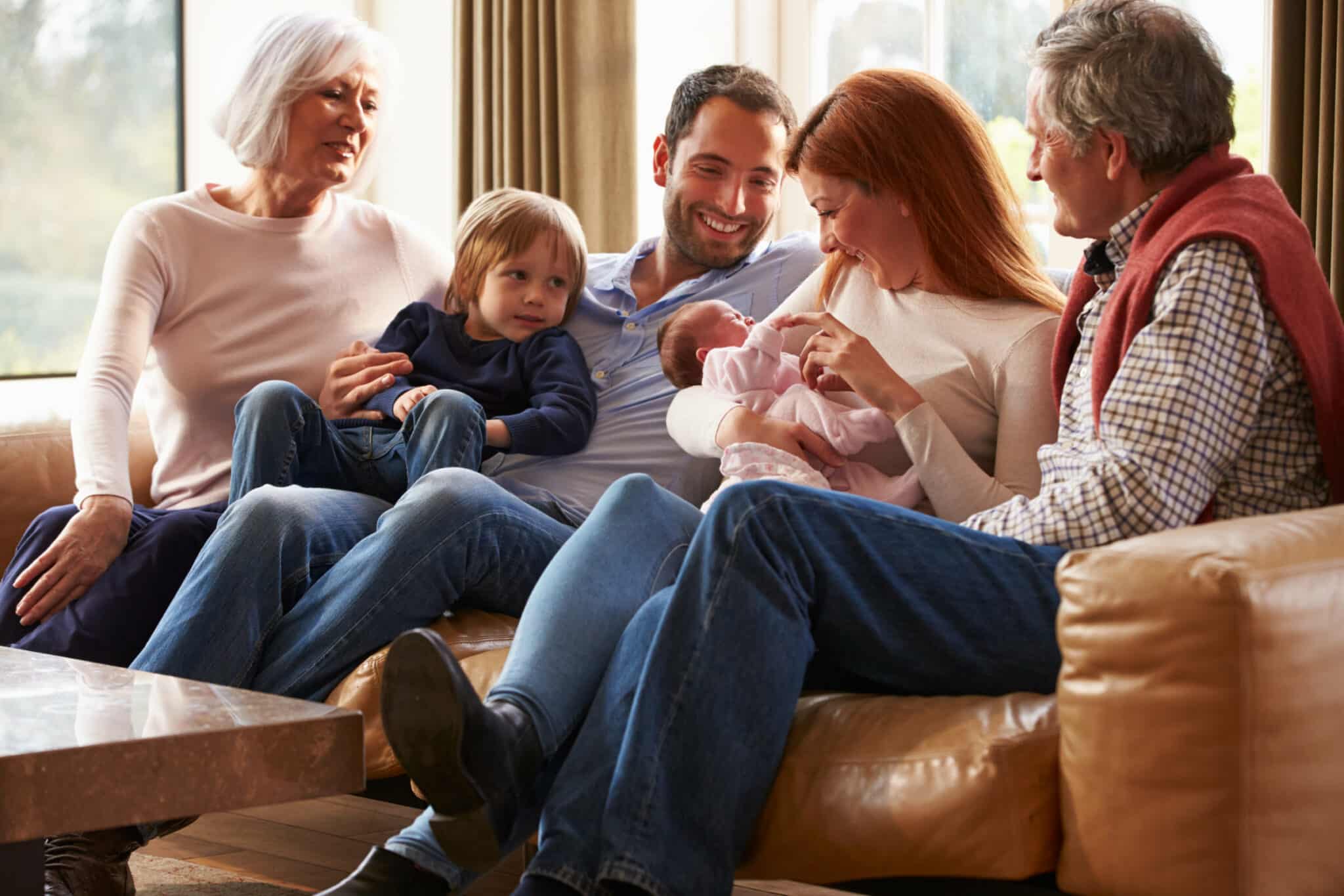 Multigeneration family sitting on sofa with newborn baby.